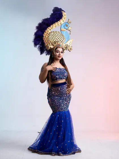 A majestic blue sequin mermaid gown paired with an elaborate peacock-themed headpiece for a truly unforgettable look.