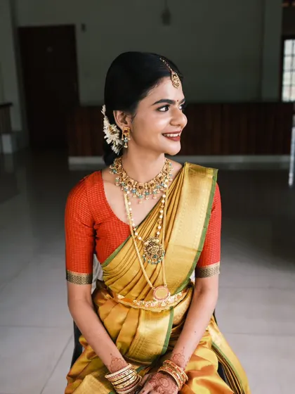 A seated portrait of the bride. Her makeup is flawless, and her hair is styled in a neat bun with fresh flowers, a classic choice for South Indian brides.
