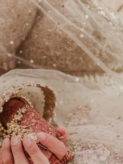 A close-up of the bride and groom holding hands, focusing on the intricate details of her sleeve and henna.