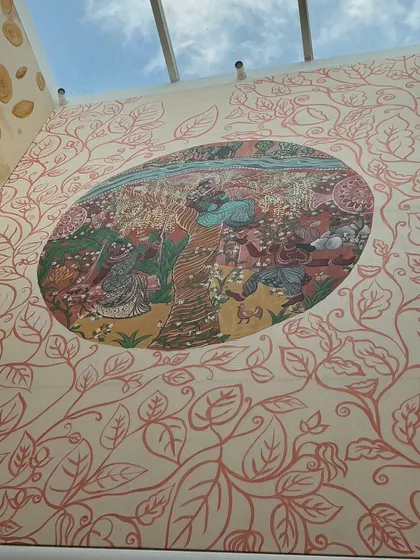 An upward-looking view of the installed "Mullai" panel, with its surrounding pattern of copper-colored leaves. The skylight above illuminates the earthy tones of the forest scene.