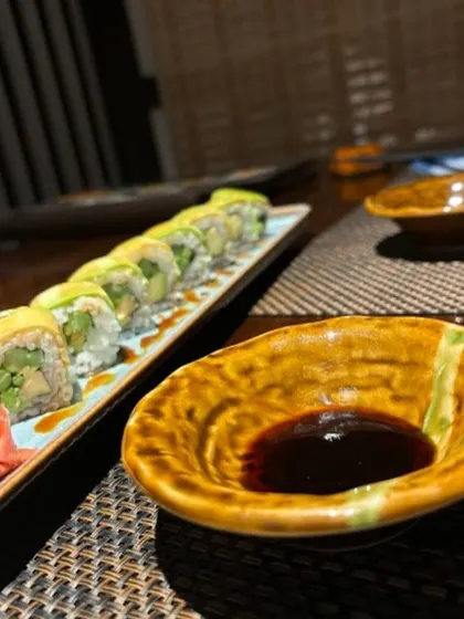 Our vegetarian Dragon Roll, featuring asparagus and cucumber wrapped in creamy avocado. It is served with soy sauce, pickled ginger, and wasabi for a complete and satisfying flavor experience.