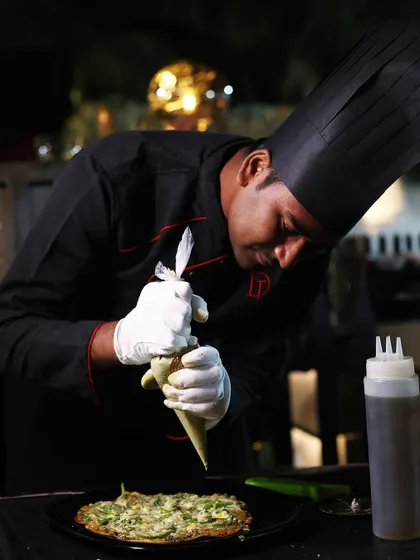 The final, artful touch. A chef carefully pipes a garnish onto a freshly made dish, demonstrating the attention to detail that elevates our food from simple catering to a gourmet experience.