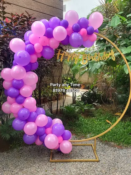 A simple outdoor balloon arch on a gold ring stand, in pink and purple.