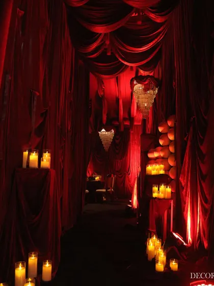 The entrance to our "Red Hue" engagement party, designed to feel like a secret, magical passage. The path is lined with clusters of pillar candles, casting a warm glow on the velvet drapes.