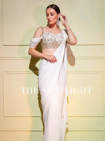 An angelic white drape saree with a structured, embroidered corset blouse. The off-shoulder drape adds a touch of ethereal grace.