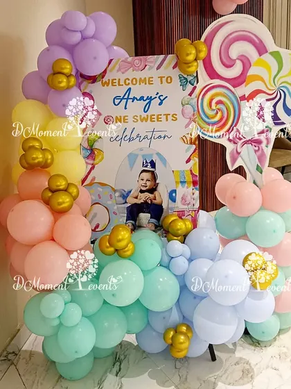 A welcome sign for a "One Sweet Celebration," surrounded by pastel balloons and giant lollipop props.