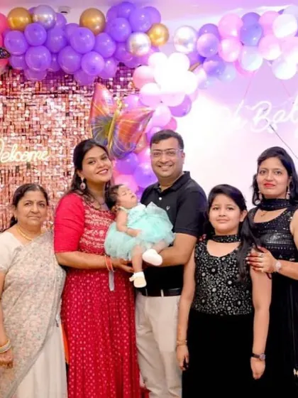 A family poses for a photo at a butterfly-themed baby welcome party. The backdrop features a pink sequin wall and a pastel balloon arch.