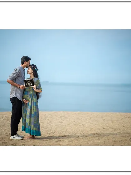 A serene beach portrait of a couple holding their sonogram picture, with the dad-to-be placing a gentle kiss on his partner's forehead.