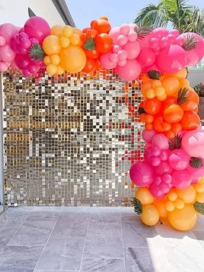 This vibrant balloon arch is perfect for daytime outdoor events like pool parties or brunches. The mix of bright pink, orange, and yellow balloons against a gold shimmer wall creates a fun and tropical feel.