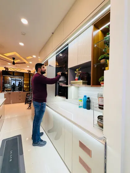 A final look at a completed kitchen in a Nirala Estate project. The design includes off-white cabinets, a built-in microwave, and open shelves, creating a balanced and functional workspace.