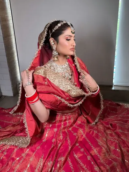 A seated pose in the red silk lehenga, showing the beautiful drape of the dupatta and the traditional bridal jewellery.