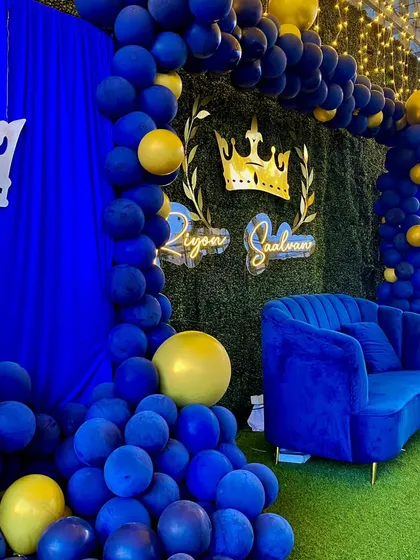 A regal blue and gold prince theme. The greenery wall is accented with a gold crown, and the space is filled with royal blue balloons and a matching velvet sofa.