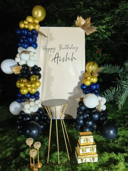 A simple and elegant outdoor setup for Aishah's birthday. This design features a clean white backdrop framed by balloon arrangements in navy, black, white, and gold for a modern and chic look.