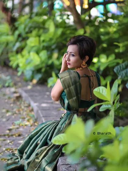 A creative shot from the back, using the natural foliage to frame the subject and showcase the details of her hairstyle and saree.
