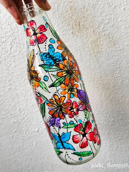 A close-up of a glass bottle painted with a vibrant garden of flowers and butterflies. This custom piece was sent to a client in Singapore.