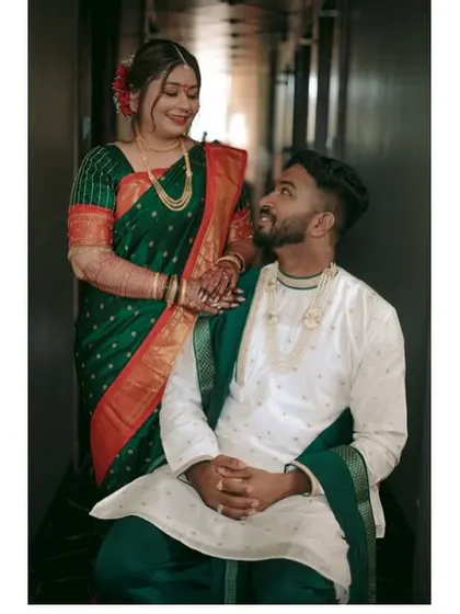 A sweet portrait of the couple, with the groom seated and the bride standing by his side, showcasing their traditional Maharashtrian wedding clothes.