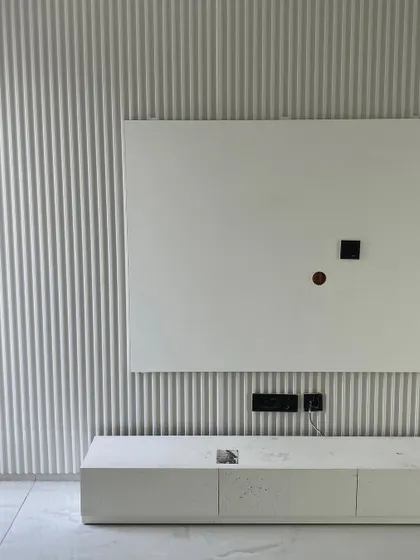 A close-up of a minimalist TV unit setup, with a fluted wall panel behind a simple white console, showcasing clean lines and subtle texture.