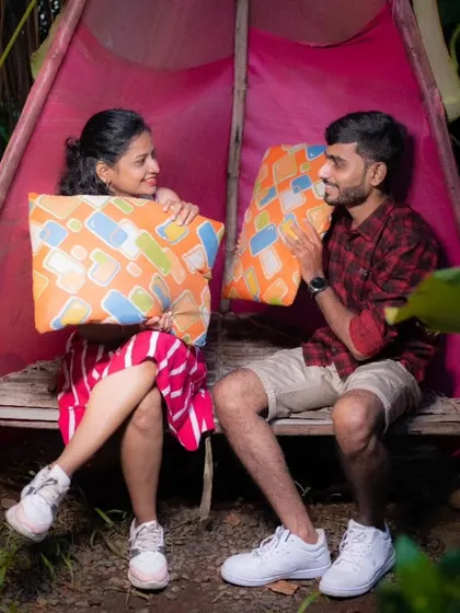 A playful pre-wedding moment where a couple sits in a rustic tent, holding up pillows and sharing a laugh.