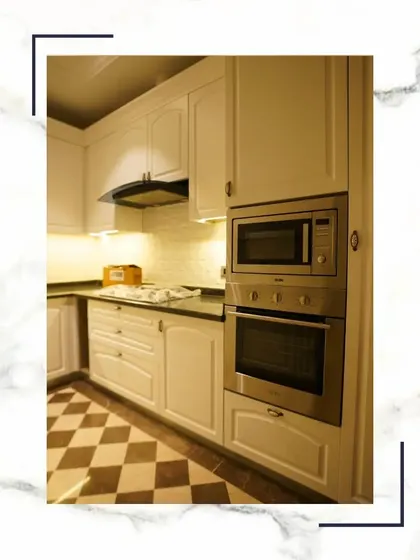 Where culinary artistry meets architectural excellence. This kitchen features white classical cabinets, a modern chimney, and built-in appliances, all set against a stylish checkerboard floor.