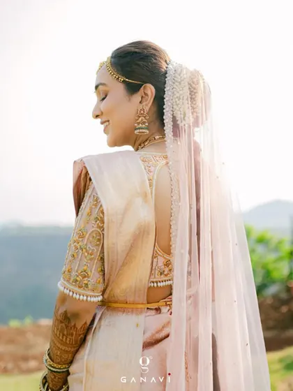 The back view of Dr. Poojita's stunning bridal look. Her custom blouse features temple-inspired embroidery and a pearl-drop border, perfectly complementing her pastel saree and intricate hair adornment.