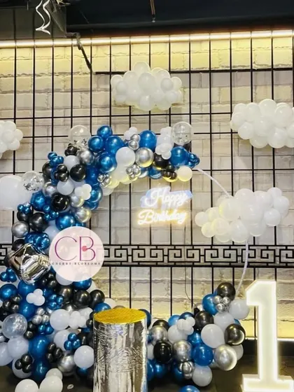 A full shot of our popular cloud-themed birthday decor. This setup is perfect for first birthdays, featuring a crescent-shaped balloon arch, a light-up number '1', and a neon 'Happy Birthday' sign for that perfect photo opportunity.