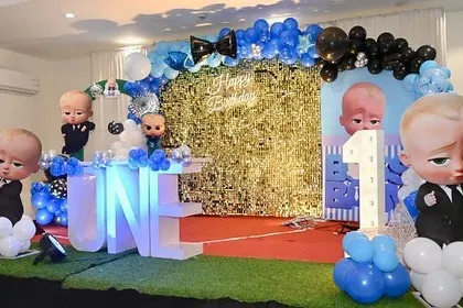 A Boss Baby first birthday stage with a gold shimmer wall. The setup includes multiple character cutouts and a "ONE" table.