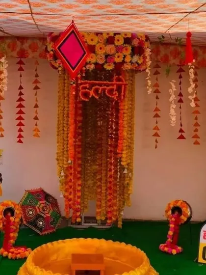 A creative Haldi setup with a canopy of hanging marigold garlands and fun "Haldi 0 km" milestone signs.