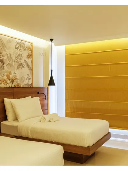 The twin bed configuration in another room, showing how the tropical-inspired wallpaper and warm yellow tones create a cohesive design language throughout the hotel.