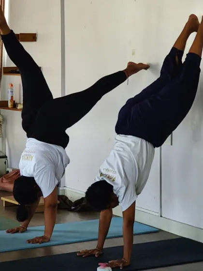 The journey from student to teacher involves overcoming challenges. Here, TTC students practice wall-supported handstands, building the strength and confidence needed to master inversions and guide others safely.