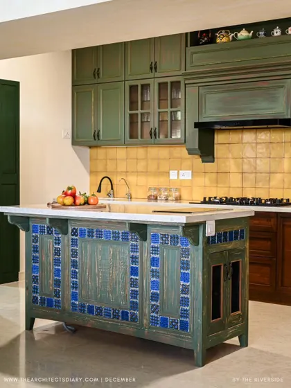 A full view of the "Colors of Goa" kitchen, with its distressed green and blue island, yellow tile backsplash, and antique-style cabinetry.