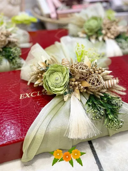 A beautifully wrapped gift box in red, adorned with a handcrafted bouquet of green and gold. This is a perfect example of how I handle individual gift wrapping with a luxurious touch.