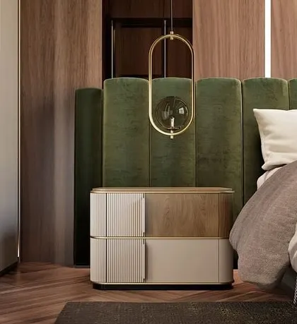 A bedside table combining veneer detailing with a painted finish, set against a deep green velvet headboard. The piece is elevated by stainless steel feet and handles in a polished gold finish.