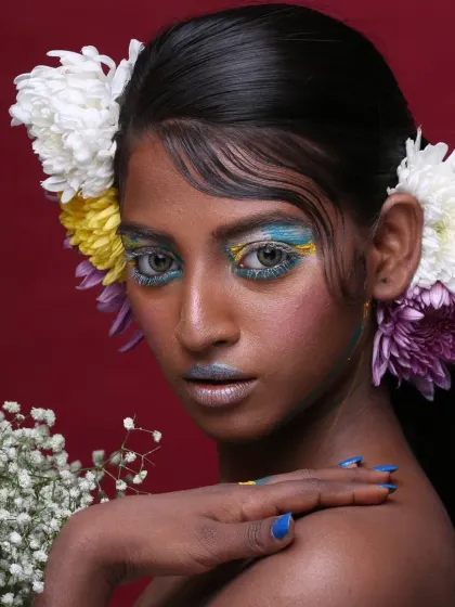 A direct gaze from the model, showing the full impact of the colorful, artistic eye makeup against the vibrant red background.