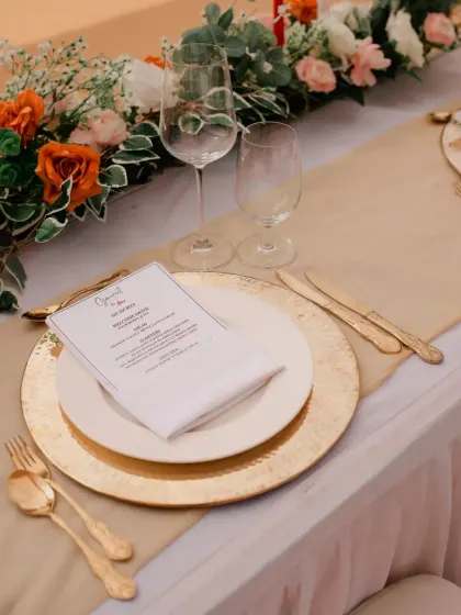 An elegant table setting with gold charger plates, custom menus, and a beautiful floral runner for a sophisticated wedding lunch.