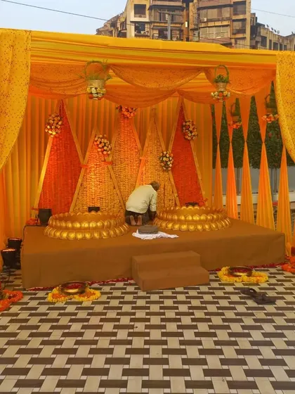 This is a full Haldi stage setup with a backdrop of woven marigold cones and traditional urlis for the ceremony, all tied together with beautiful orange and yellow drapes.