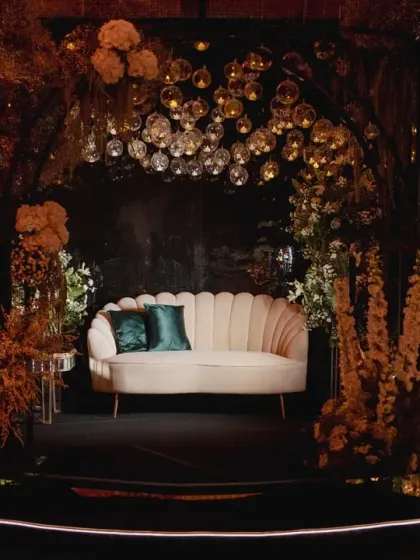 A beautifully styled photo booth area for the engagement party. The backdrop of hanging glass orbs and lush, moody florals creates a sophisticated and enchanting setting for pictures.