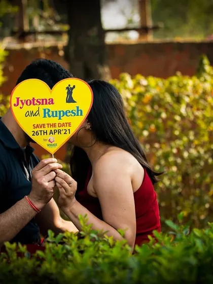 A cute and creative "Save the Date" idea, where the couple shares a kiss behind a heart-shaped sign. It’s a simple yet effective way to announce your big day.