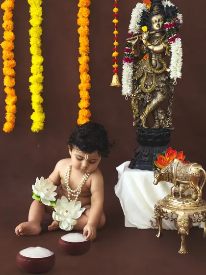 A baby Krishna playing with lotus flowers in a simple, elegant festive setup.
