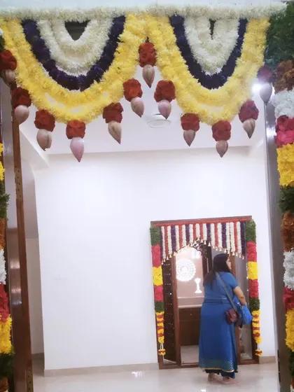 A view of the main door and the pooja room door, both decorated with matching floral garlands for a cohesive look during a housewarming.