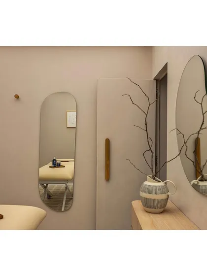 Details in the treatment area are carefully considered to enhance the sense of tranquility. Organic-shaped mirrors reflect the soft light, while a simple wooden door handle and natural branch decor add a touch of wabi-sabi inspired warmth.