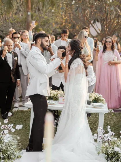 A sweet moment during the cake-cutting ceremony, with family and friends looking on with joy. This candid shot captures a classic wedding tradition in a beautiful outdoor setting.