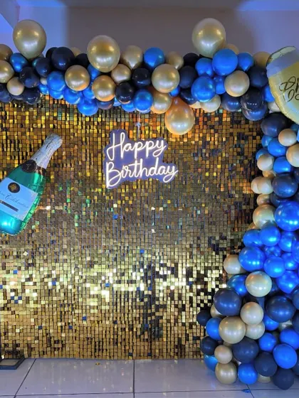 Another shot of the blue and gold birthday decoration, showing the 'Happy Birthday' neon sign glowing against the shimmer wall.