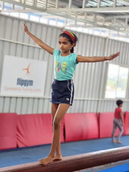 A young gymnast finds her balance on the beam, holding a pose with arms outstretched. The beam is excellent for developing focus and stability.