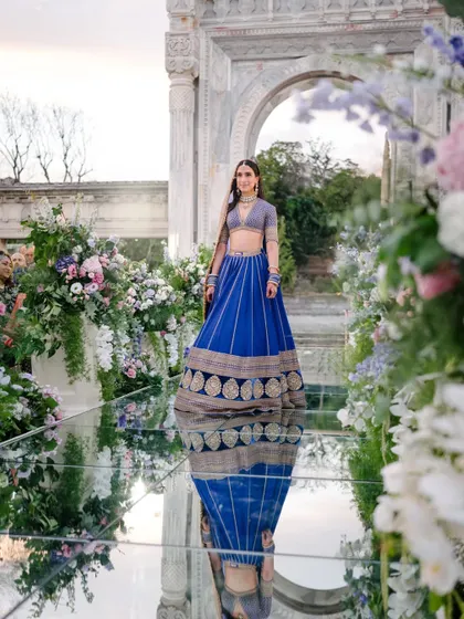 A bride's breathtaking walk down a mirrored aisle, flanked by lush floral arrangements. Her reflection creates a stunning visual, making her entrance feel ethereal and deeply romantic.