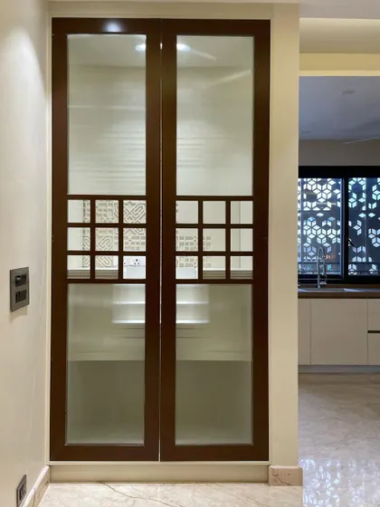 This is the home temple with its doors closed. The design features frosted glass for privacy, with a small wooden jali section that allows a glimpse inside, blending aesthetics with traditional design cues.