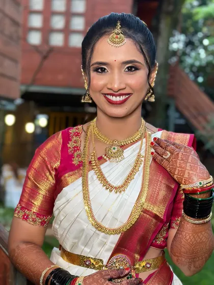 A beautiful smile from my gorgeous bride on her muhurtham. Her makeup features a classic bold red lip and subtly shimmering eyes, perfectly framed by her traditional gold jewelry and an elegant updo.