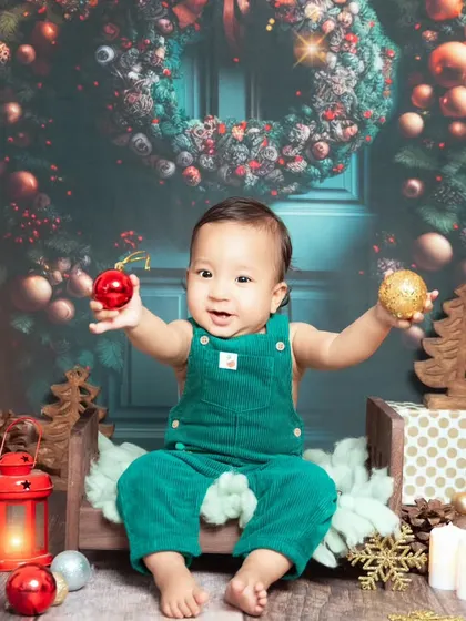 A vibrant and festive Christmas setup. This little one is ready for Santa with his green overalls and a backdrop full of holiday cheer.