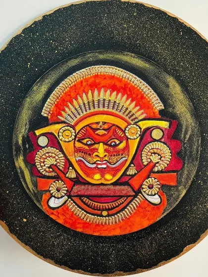 A duplicate image of the Theyyam wall plate, held to show its size and the three-dimensional quality of the painting.