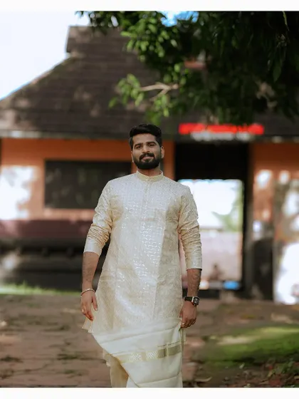 A confident portrait of the groom in front of a traditional Kerala building.