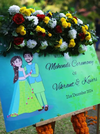 A personalized welcome sign for Vikrant and Kaveri's Mehendi ceremony, adorned with a fresh floral arrangement.